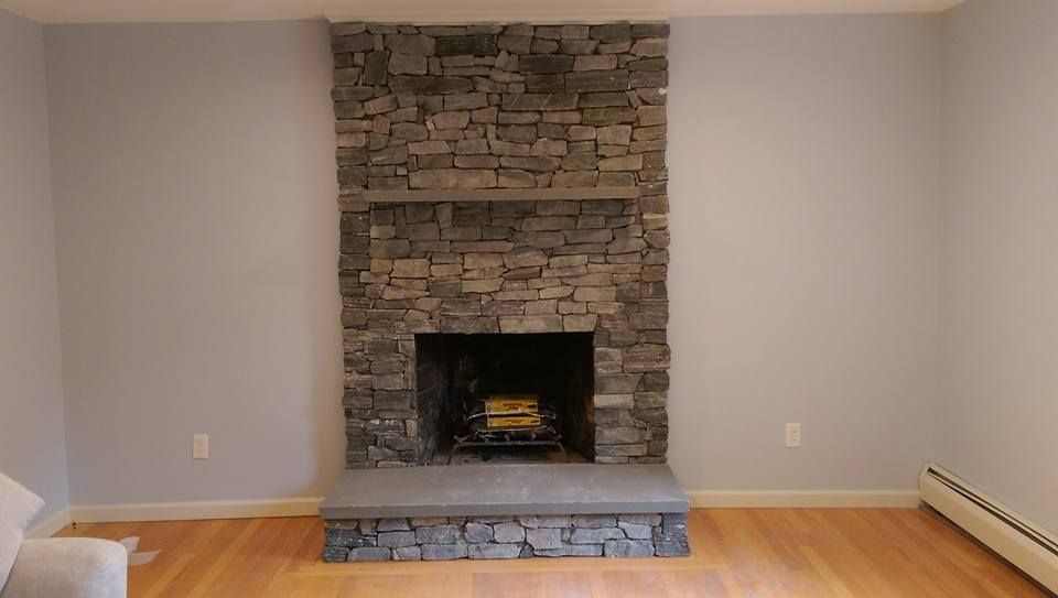 Stone fireplace centered on a light purple wall, with wooden flooring and a radiator.