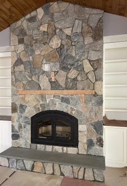 Stone fireplace with arched firebox, wooden mantel, built-in white shelves.