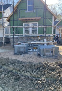Construction site with a partially built house. Scaffolding, green insulation, and stone foundation visible.