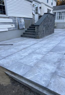 Gray paved patio and steps leading to a building with stone wall.