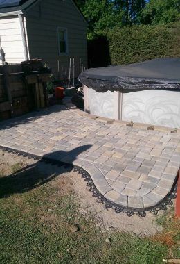 A brick patio borders an above-ground pool. Dark edging curves around the patio’s edge.