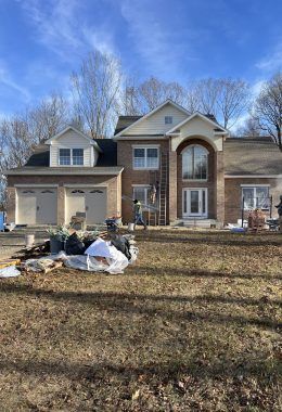 Two-story brick house under construction, with a two-car garage. A ladder and workers are visible.