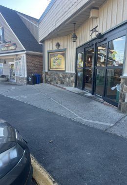 Entrance to a store with a ramp for accessibility, featuring automatic doors and stone detailing.