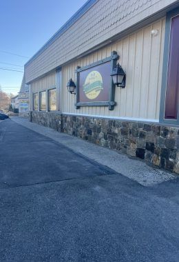 Restaurant exterior with stone facade, sign, and streetlights.