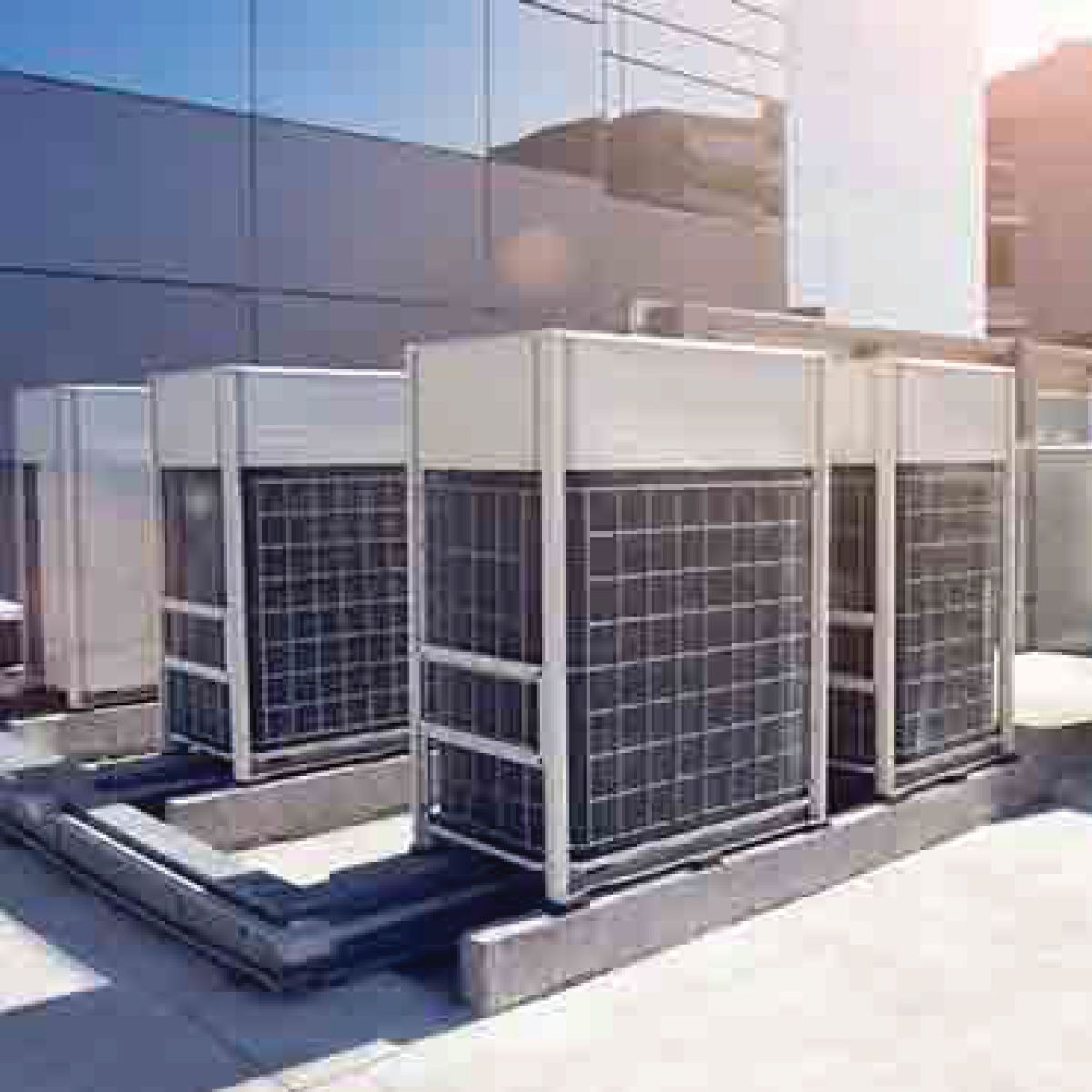Outdoor HVAC units on a building roof, silver and white with metal grates.