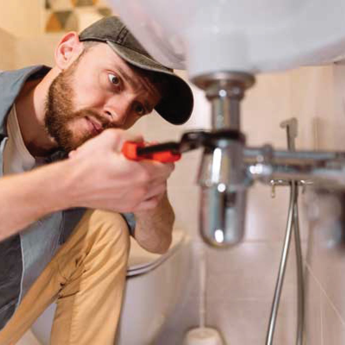 Plumber working under a bathroom sink with a wrench.