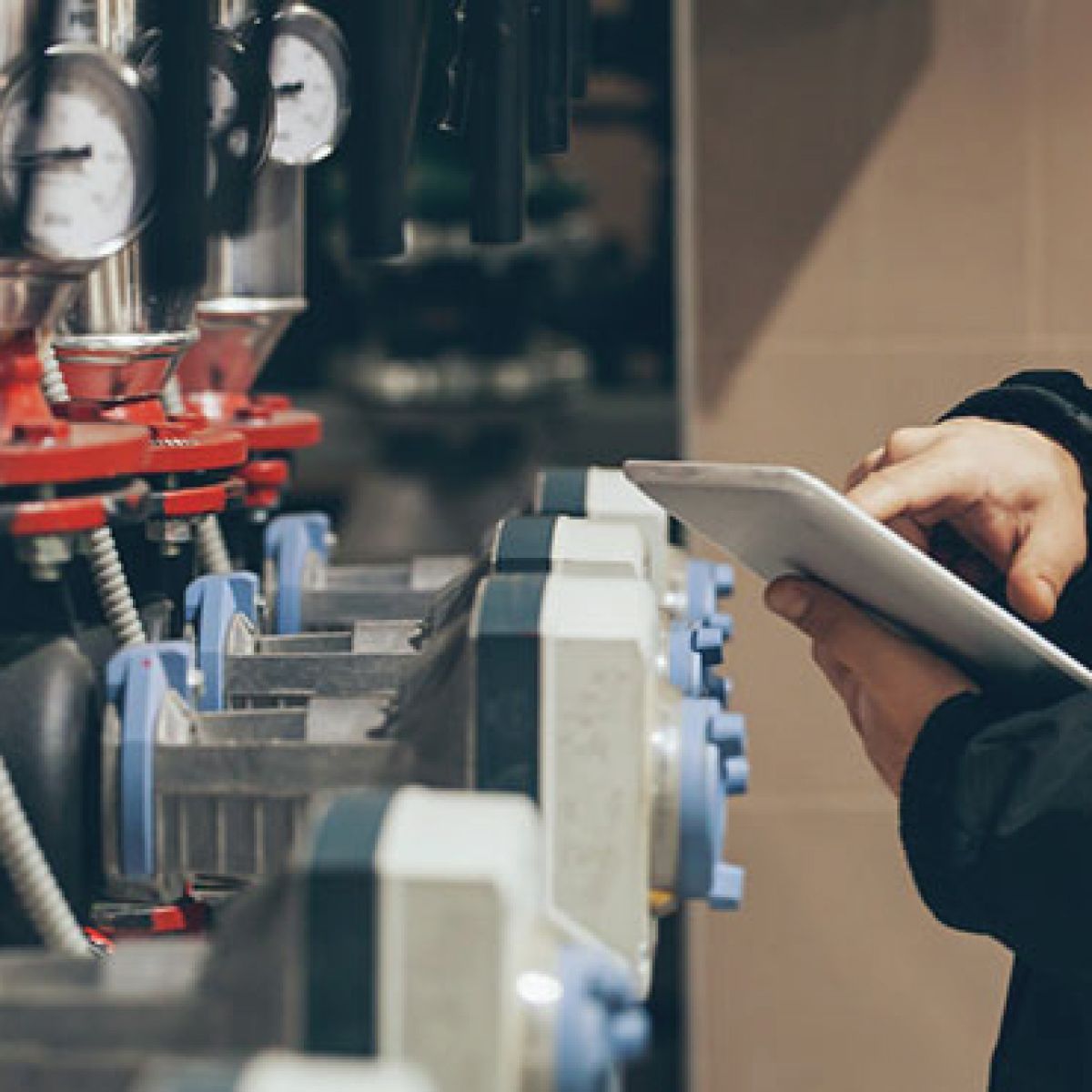 Person using a tablet to inspect industrial equipment with gauges and valves.