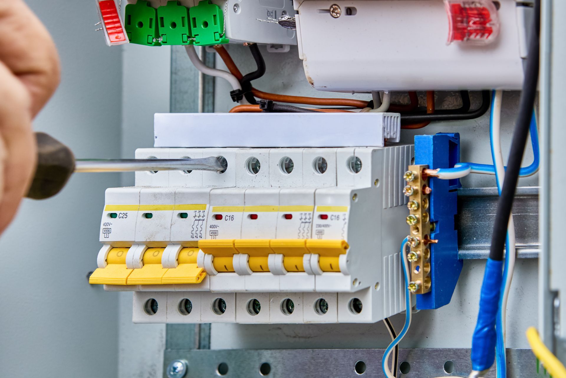 Electrician performing service maintenance on a consumer unit in an outdoor switchboard in a rural area.