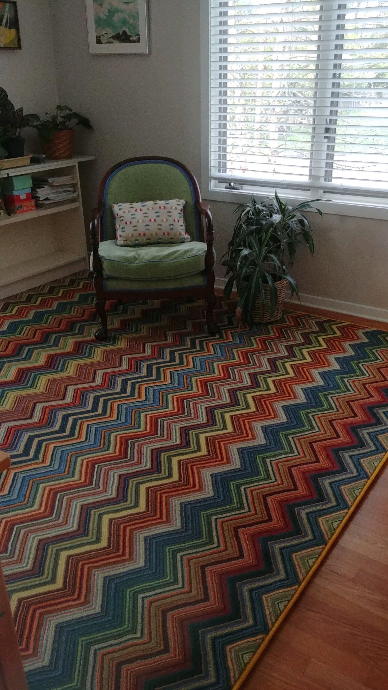Bright room with colorful chevron rug, green chair, plant, and window with blinds