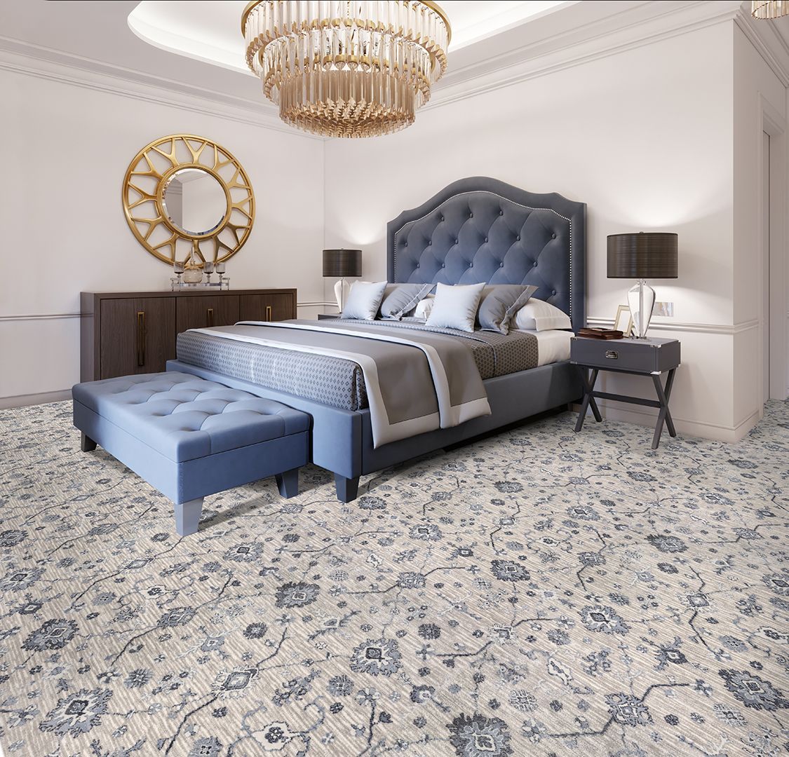 Elegant bedroom with a blue tufted bed, chandelier, and patterned rug.