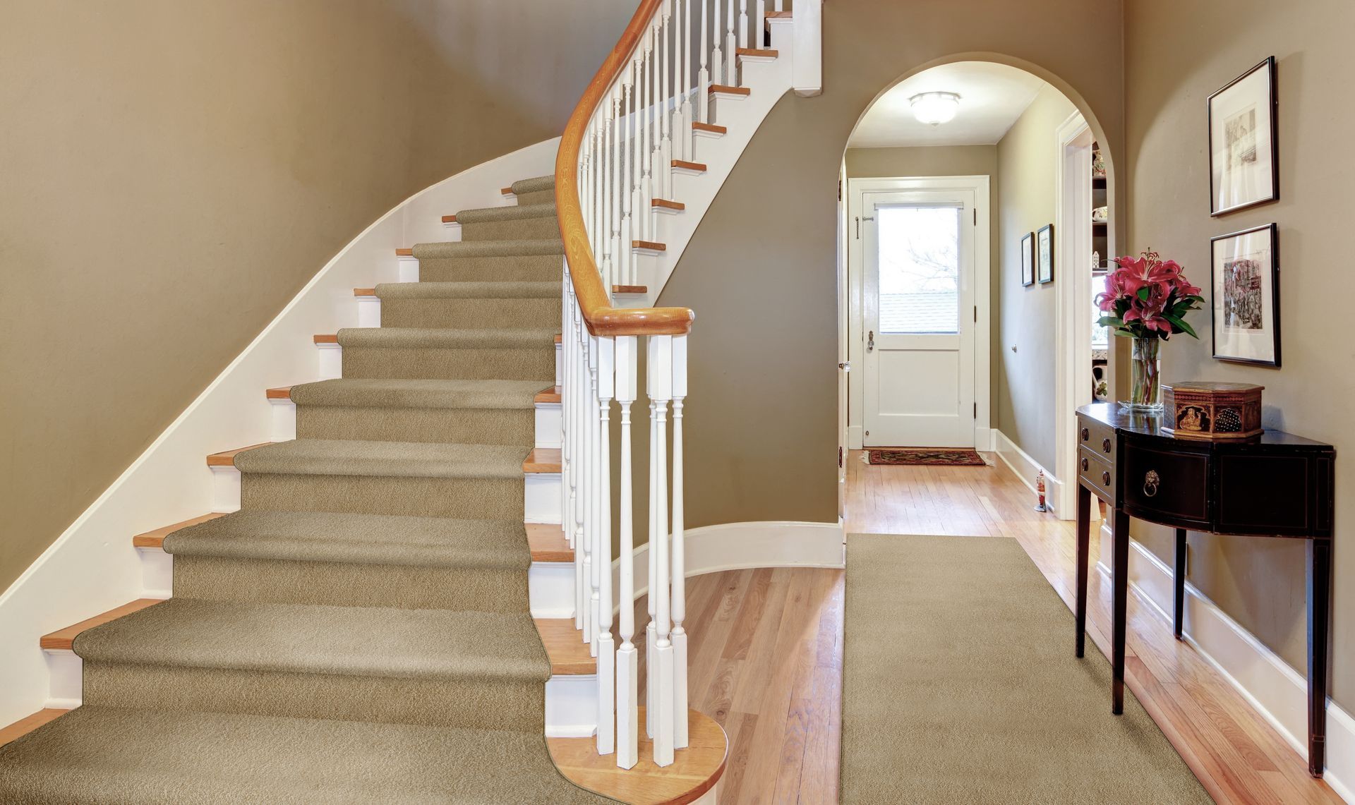 Curving staircase with beige carpet, white railing, and wooden handrail in a hallway.