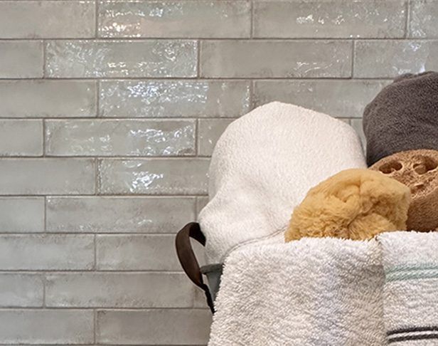 Basket of towels and sponges in front of a light gray, brick-laid tiled wall.