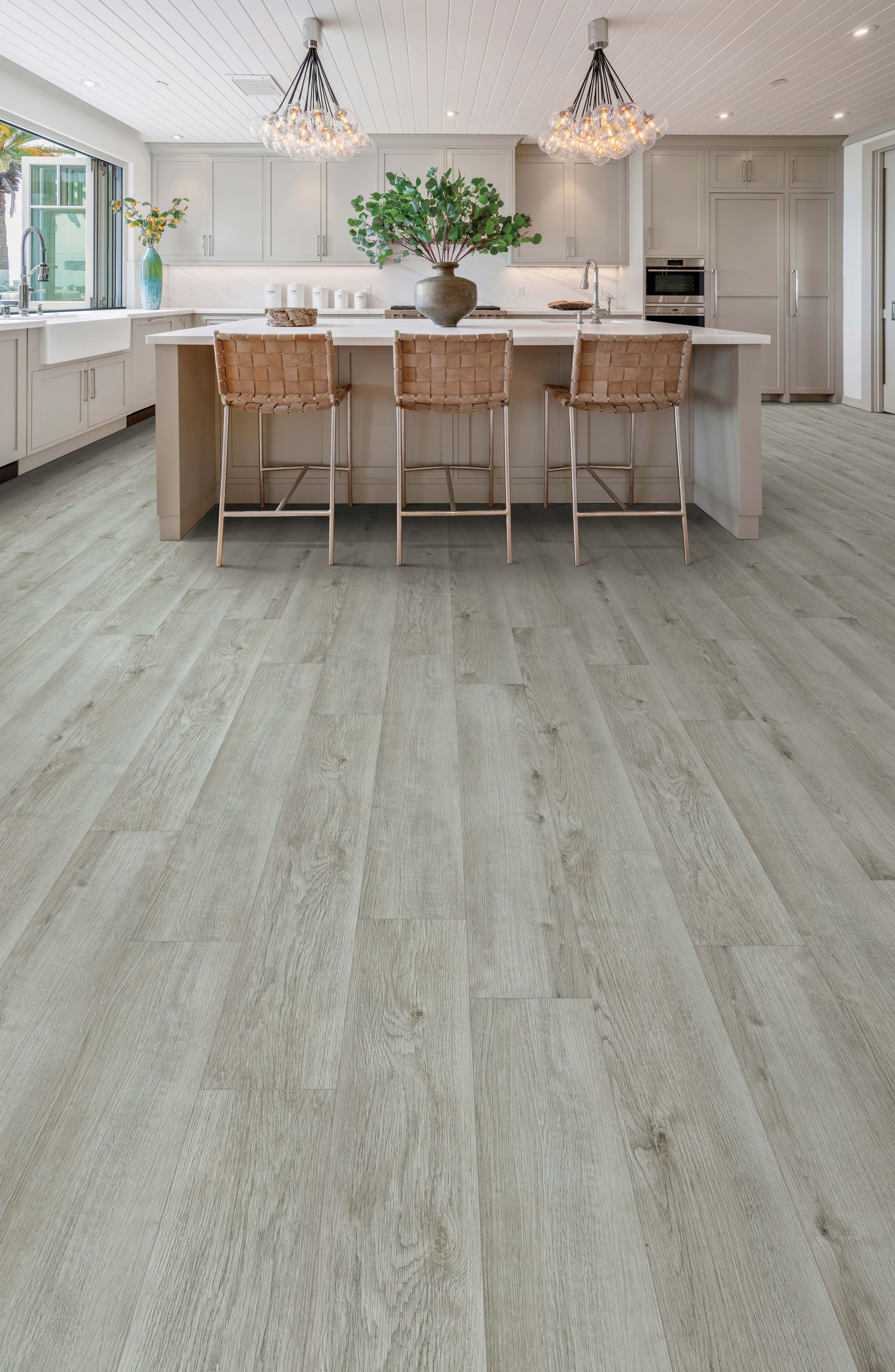 Bright kitchen with light wood island, pendant lights, and gray flooring, viewed from a long open space