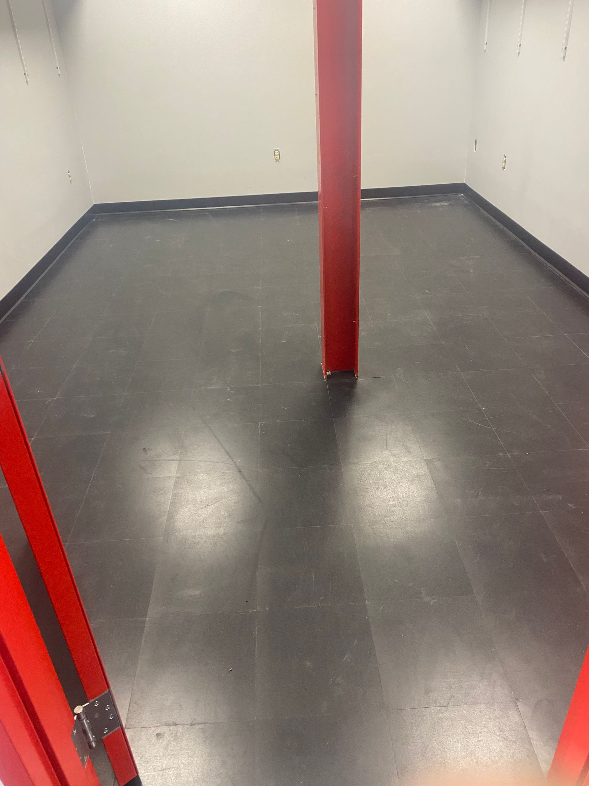 Empty gray room with red poles and dark floor, viewed from an entrance