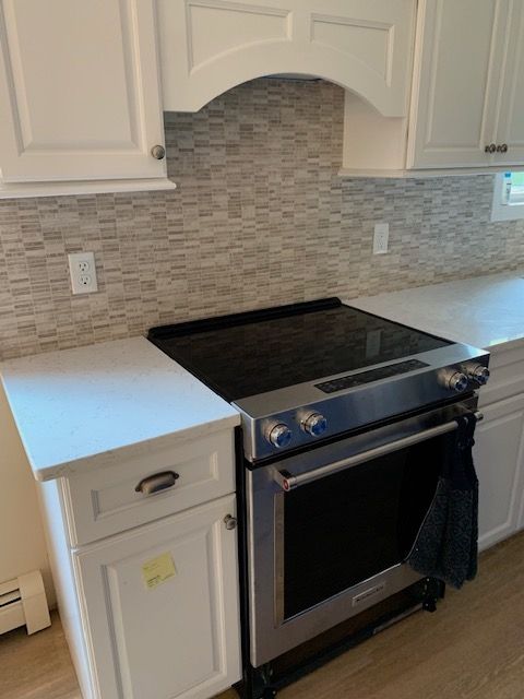 Kitchen with white cabinets, mosaic tile backsplash, and a stainless steel oven beneath a black cooktop.