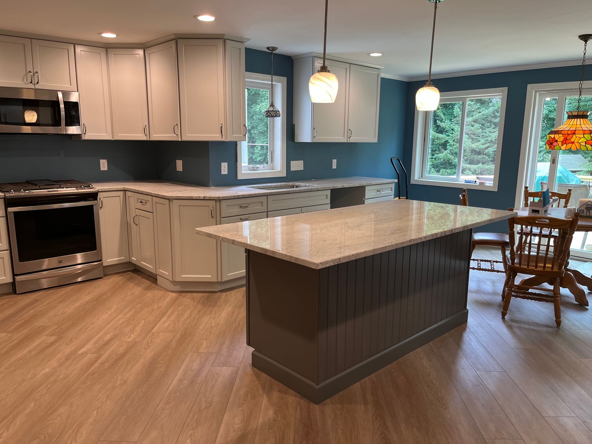 Modern kitchen with white cabinets, dark island, wood floor, and large windows by a dining area