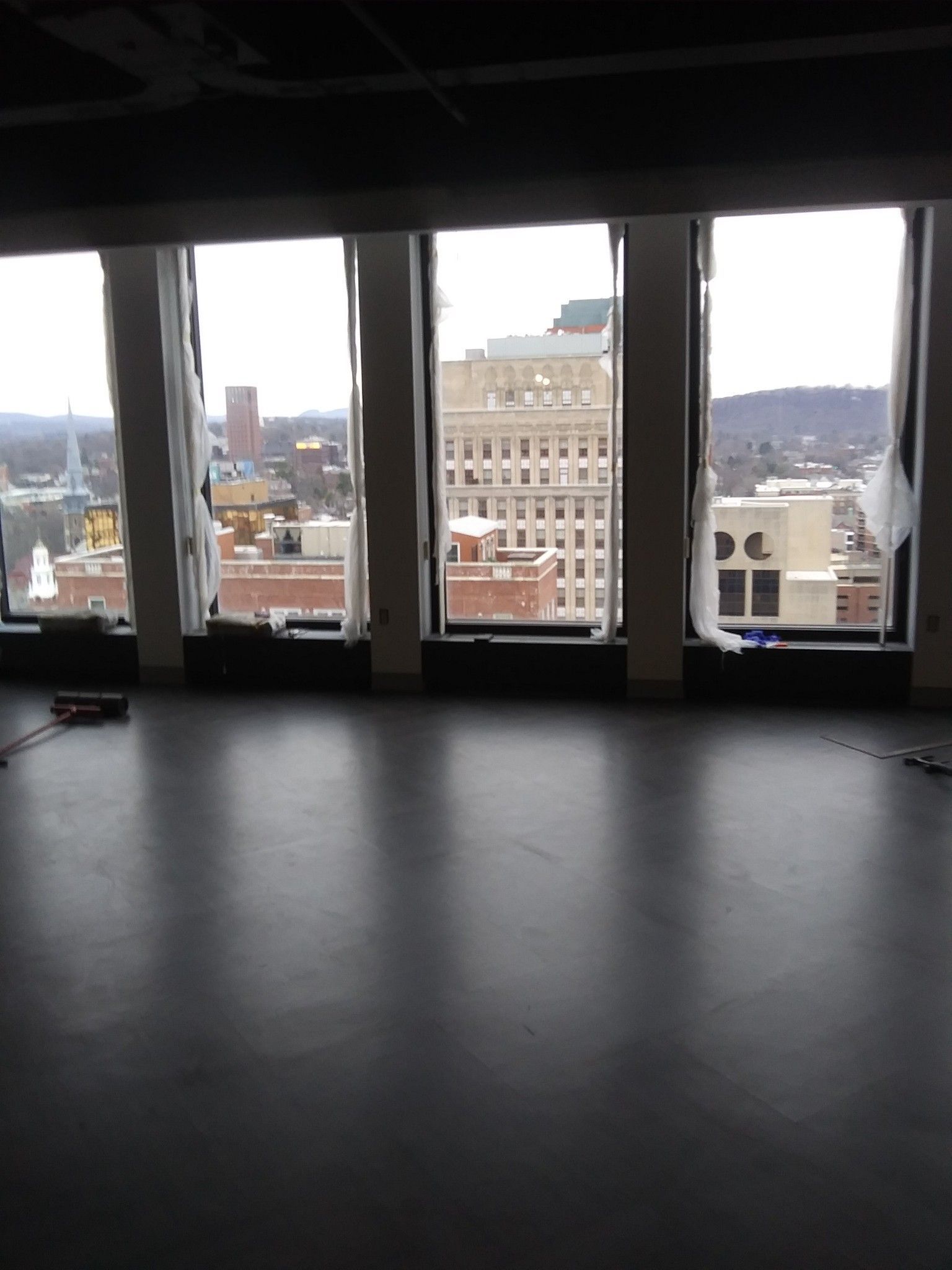 Empty room with large windows overlooking a city skyline on an overcast day