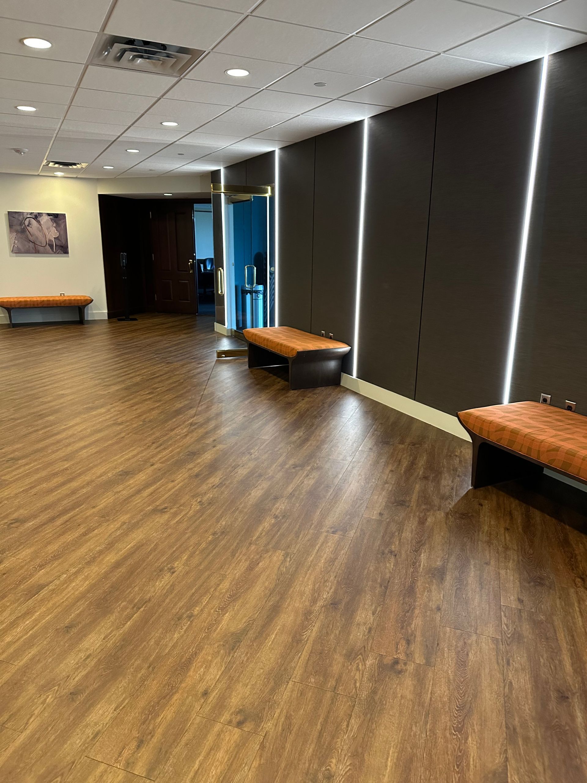 Empty hallway with wood floors, dark wall panels, and benches along the sides.