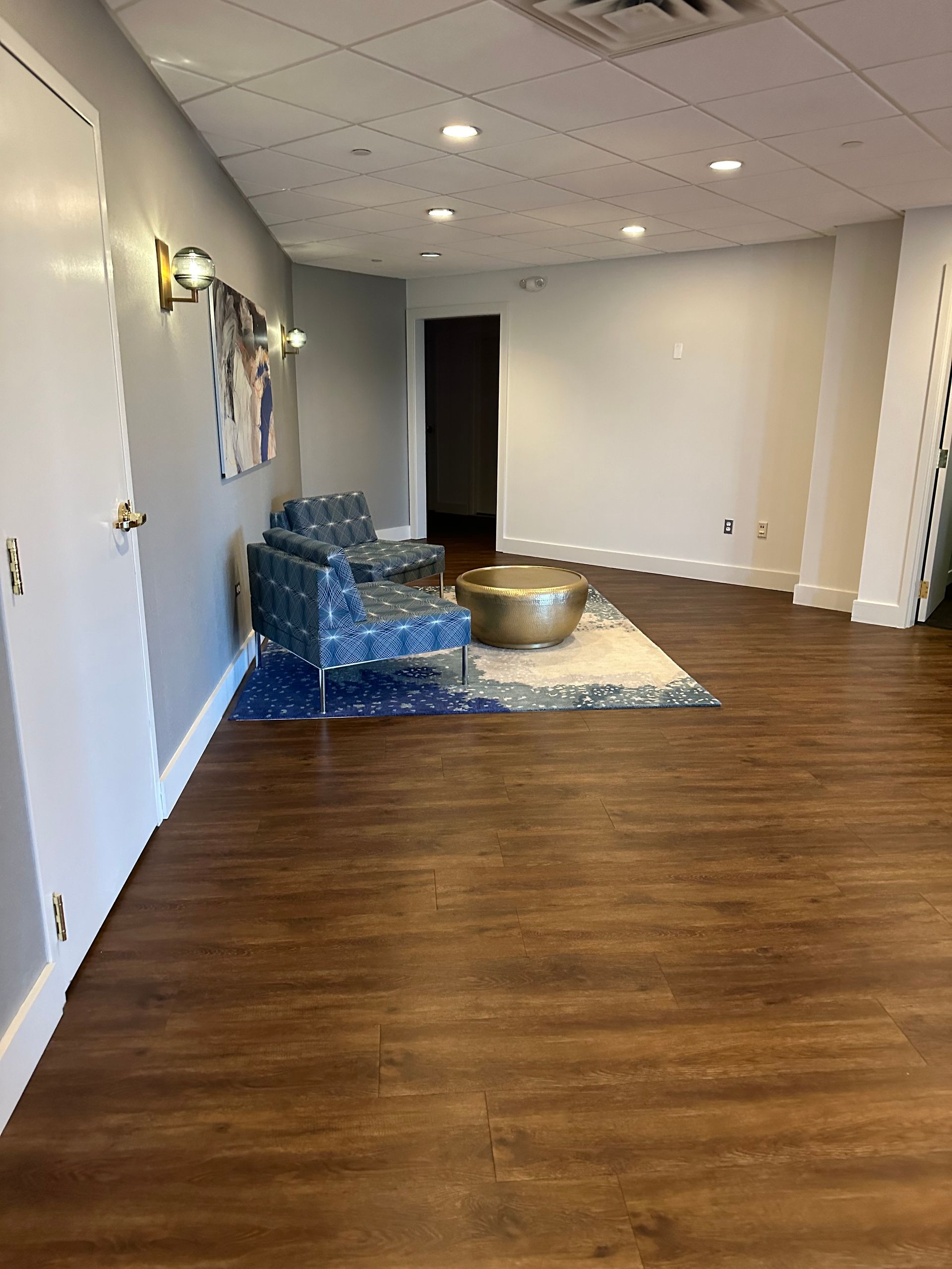 Empty room with hardwood floor, white walls, and a blue couch area on a rug near the back wall