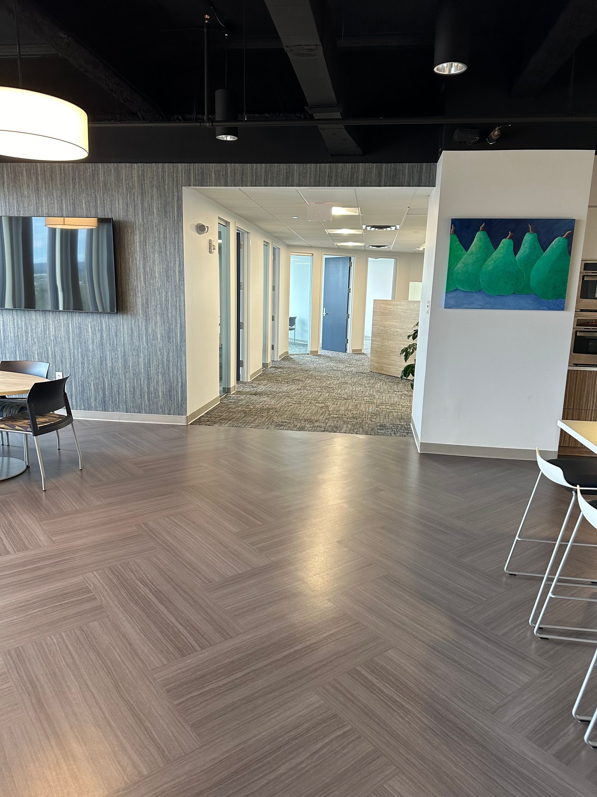 Modern office lobby with wood floor, lounge chairs, and a hallway leading to a bright workspace