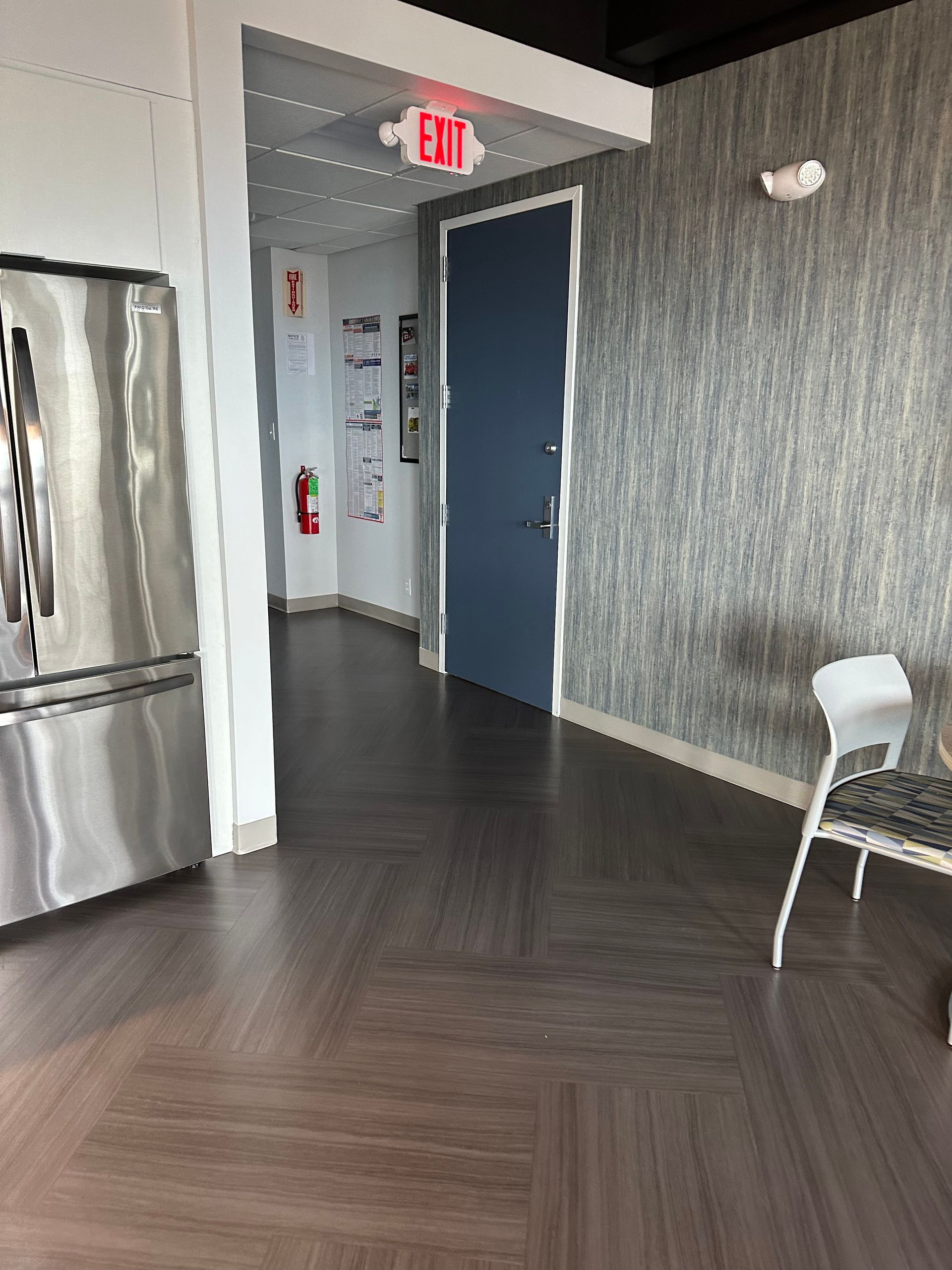 Hallway with herringbone wood floor, textured gray walls, blue door, and a metal chair near the wall