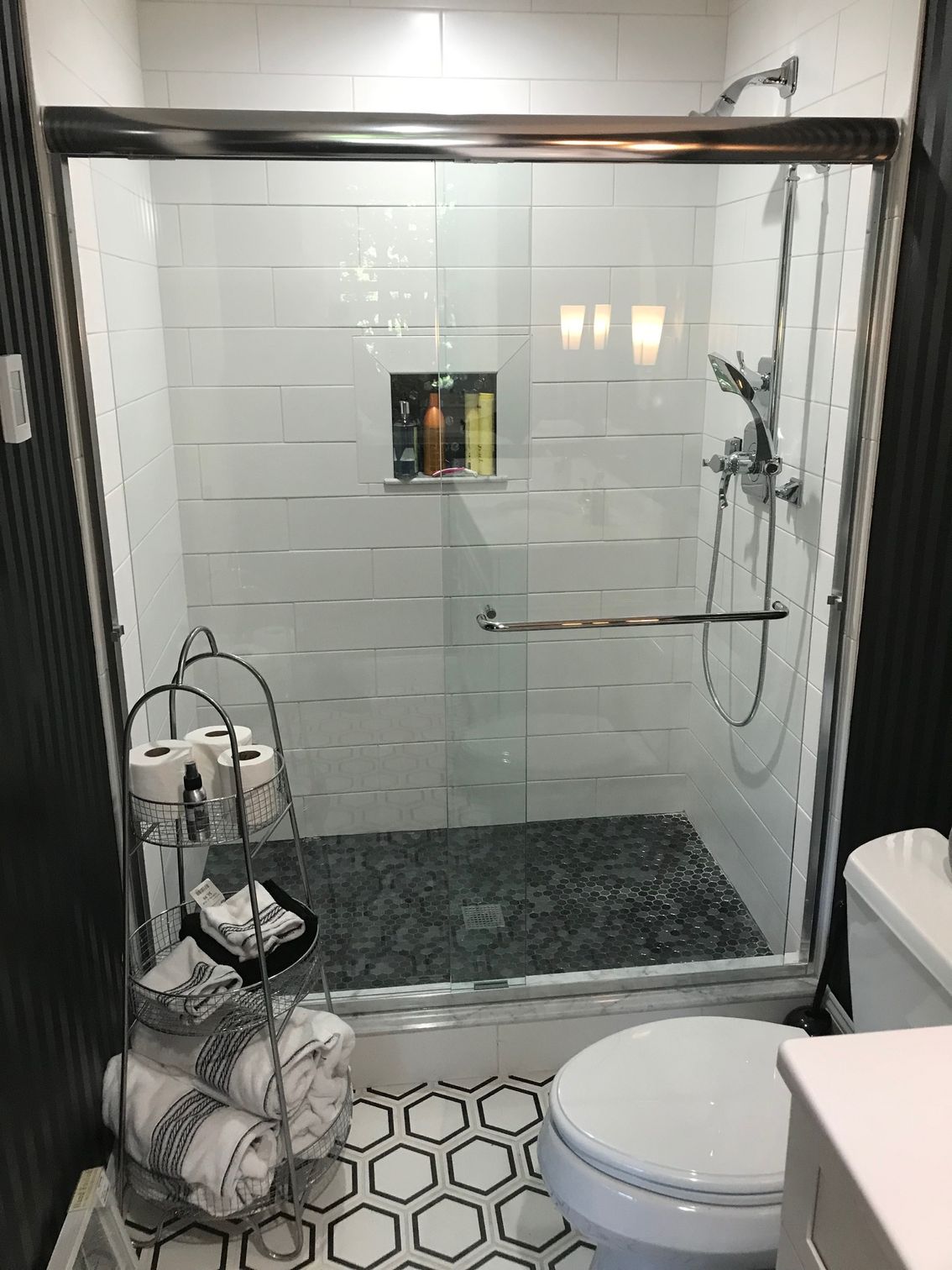 Glass shower with white tile walls and dark pebble floor, beside a toilet in a small bathroom