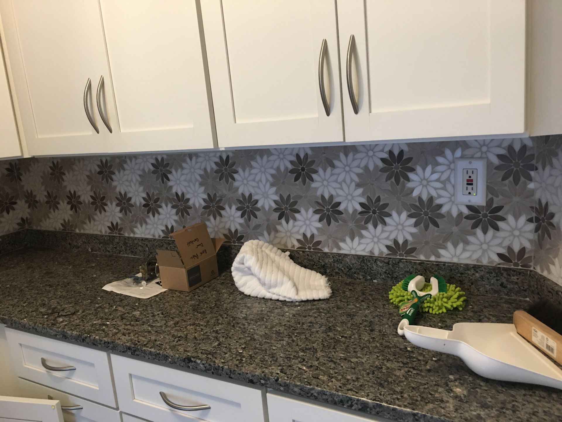 Kitchen countertop with granite surface, white cabinets, and miscellaneous items scattered on the counter