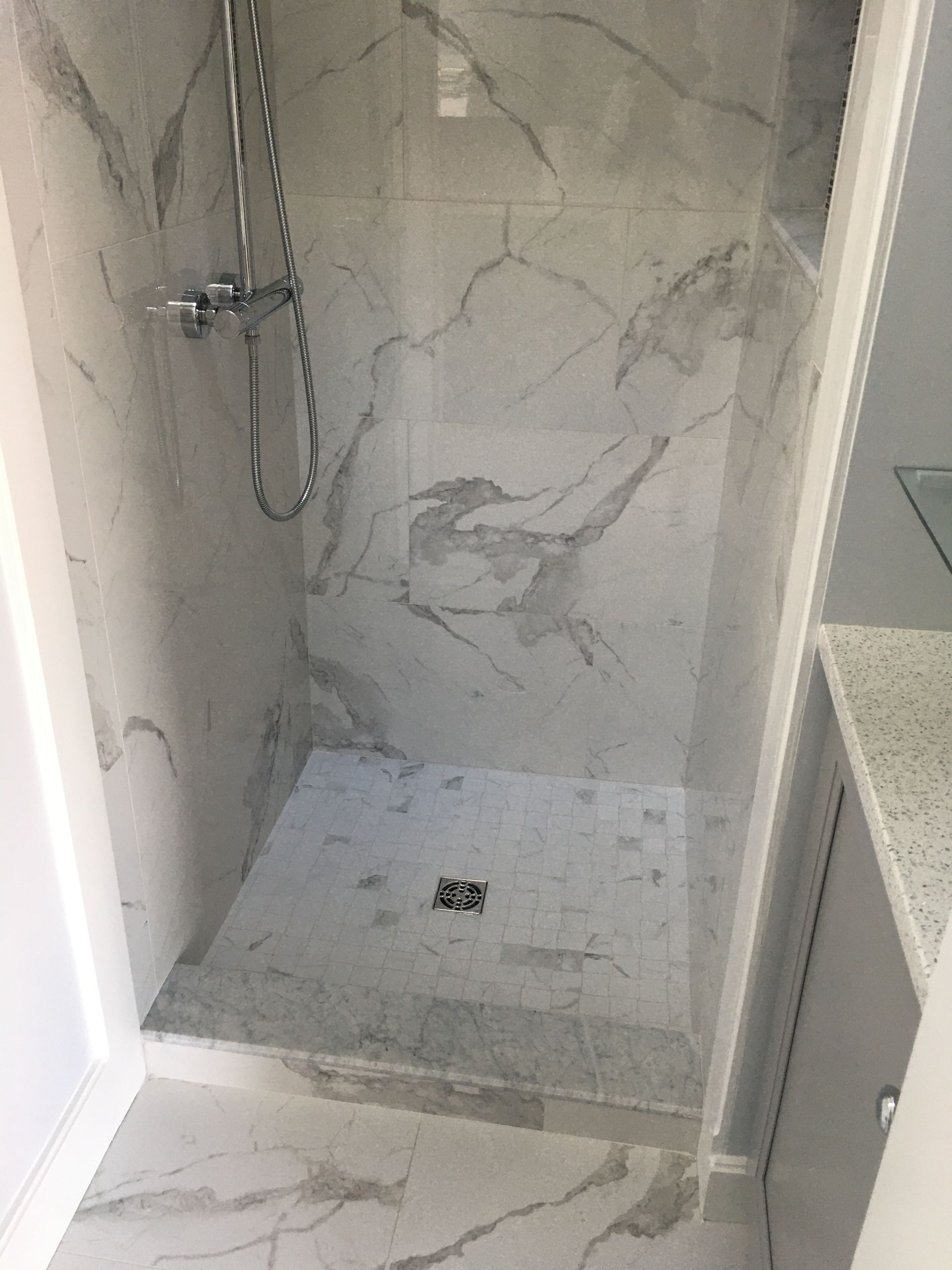 Empty tiled shower stall with marble-look walls and a shower drain.