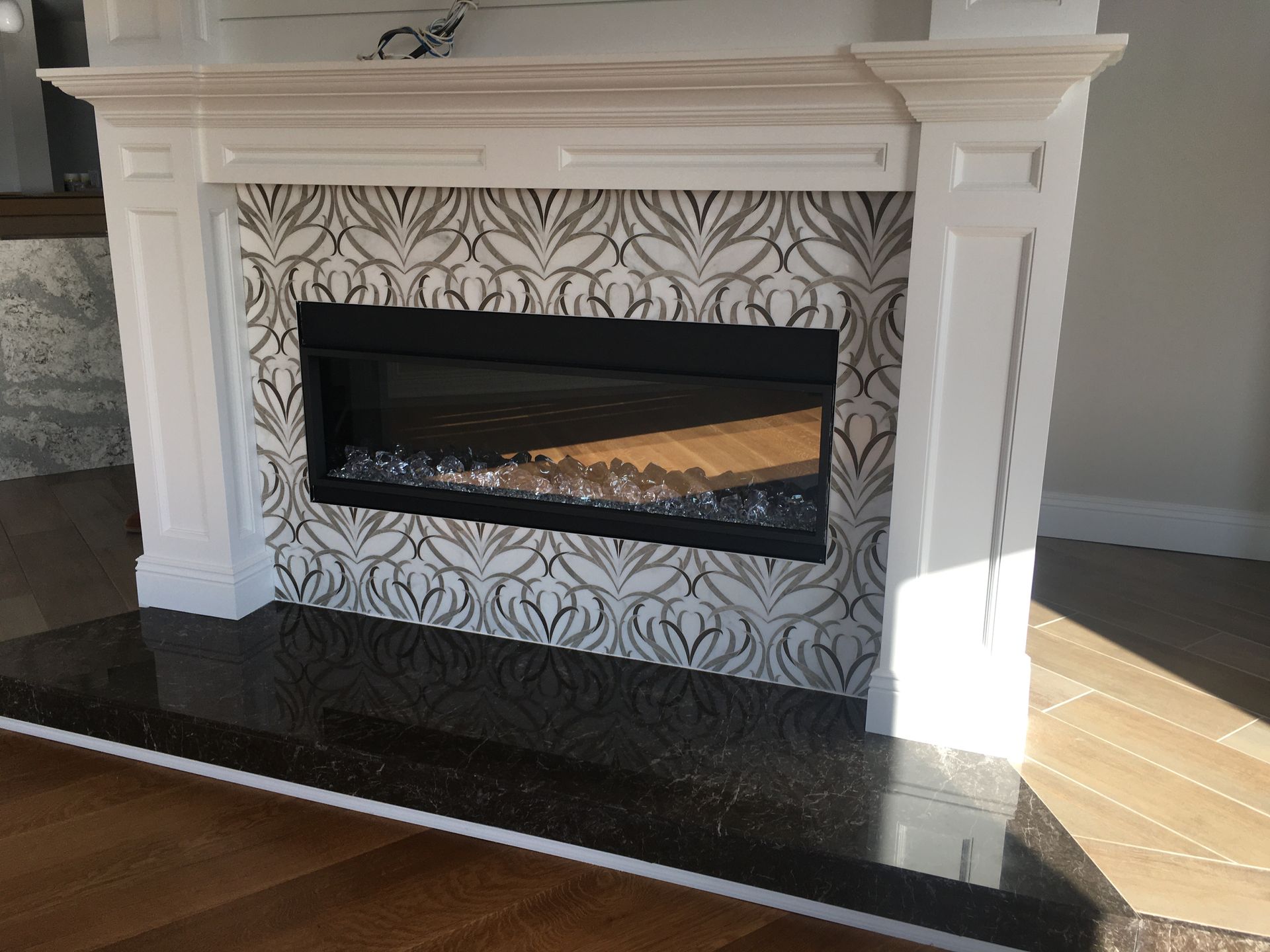 White fireplace with black marble hearth and patterned tile surround in a bright room