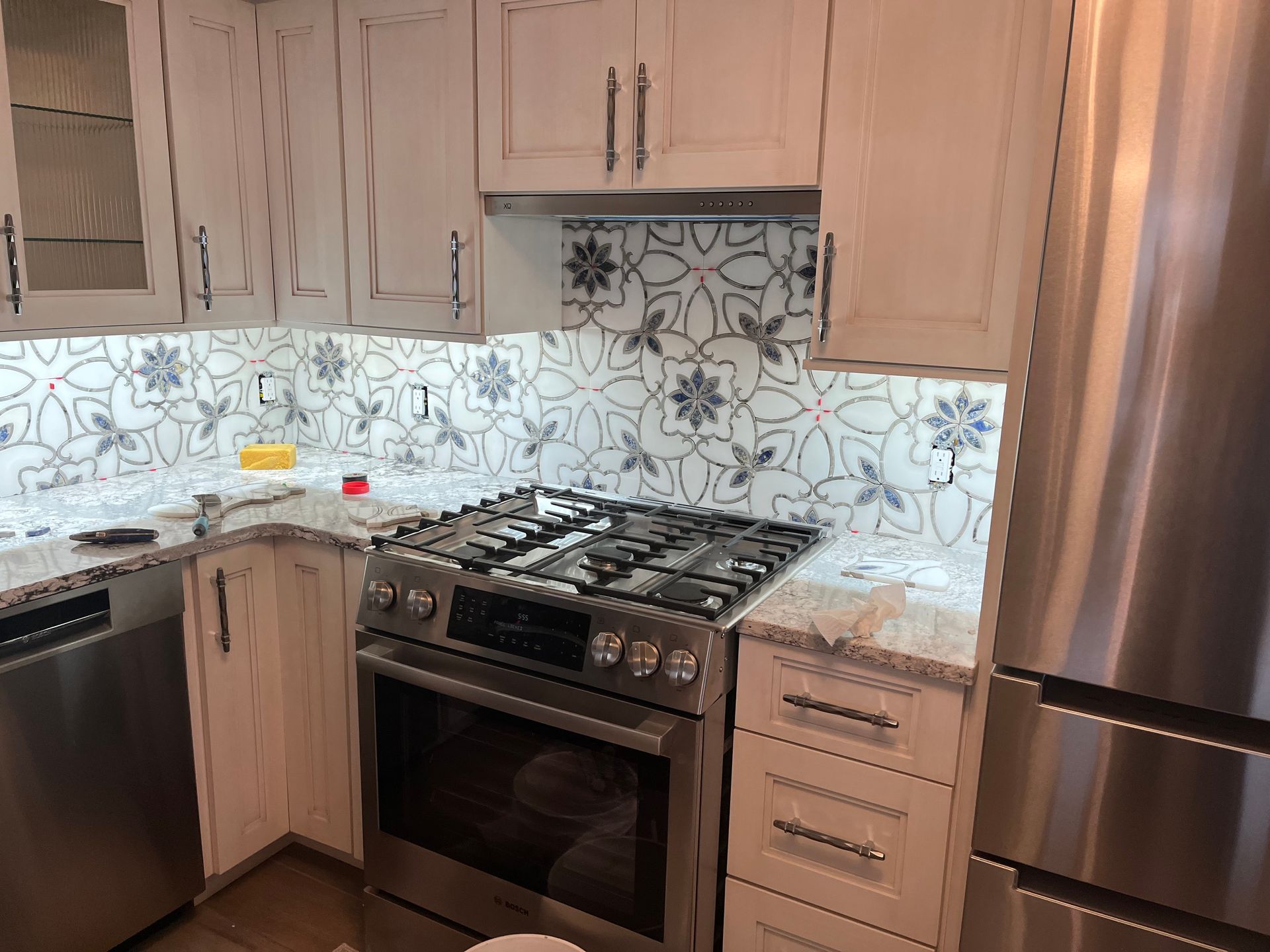 Modern kitchen with stainless steel appliances, beige cabinets, patterned white backsplash, and gas range.
