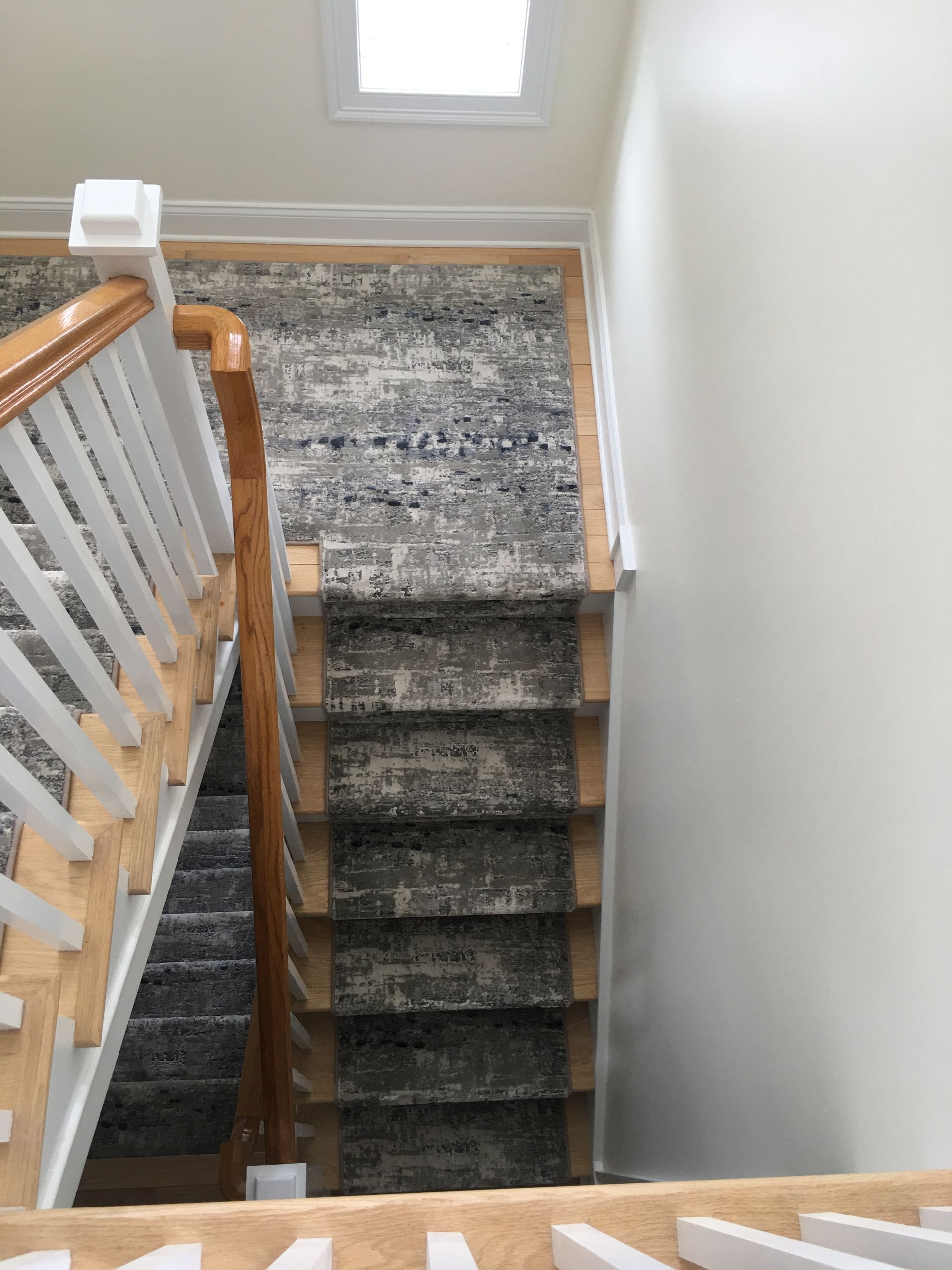 Narrow carpeted staircase with wooden and white railings beside a window.