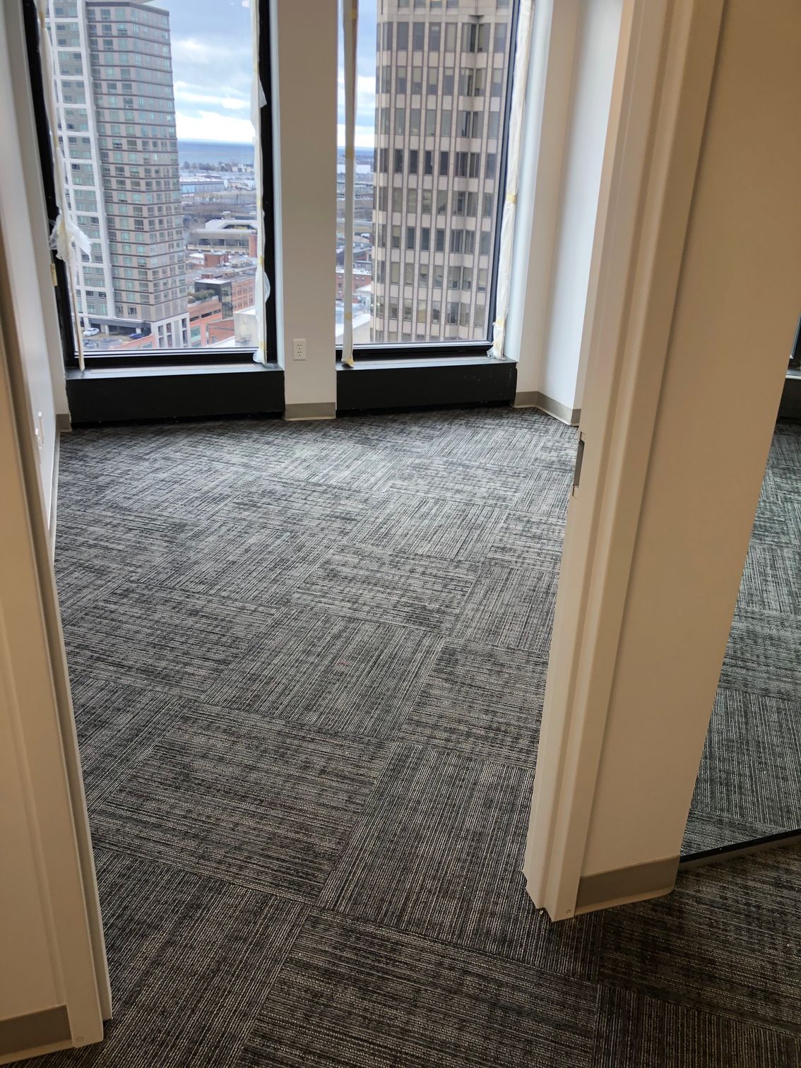 Hallway with carpeted floor leading to a large window overlooking city buildings