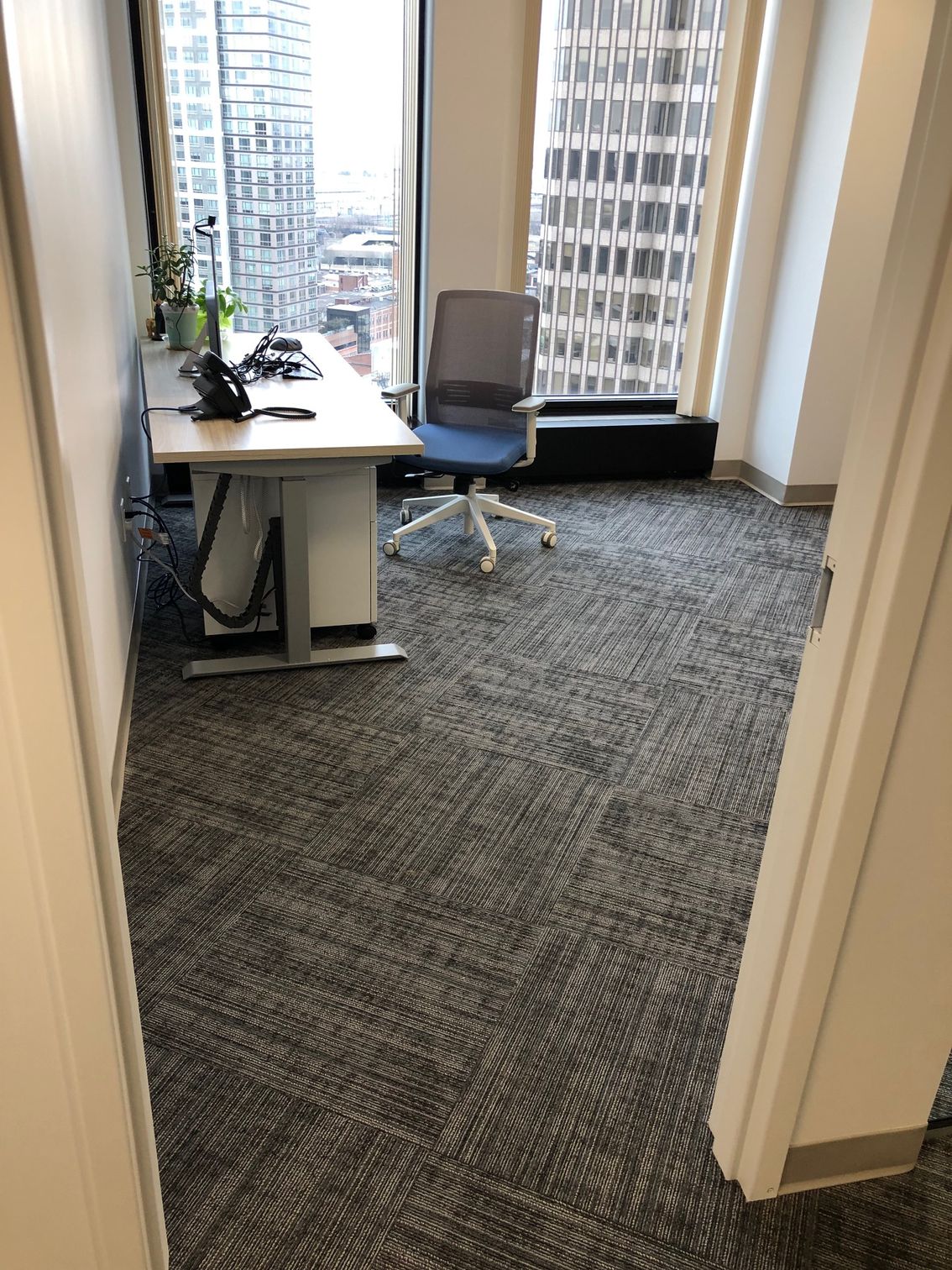 Empty office with desk, chair, and city view through large windows.
