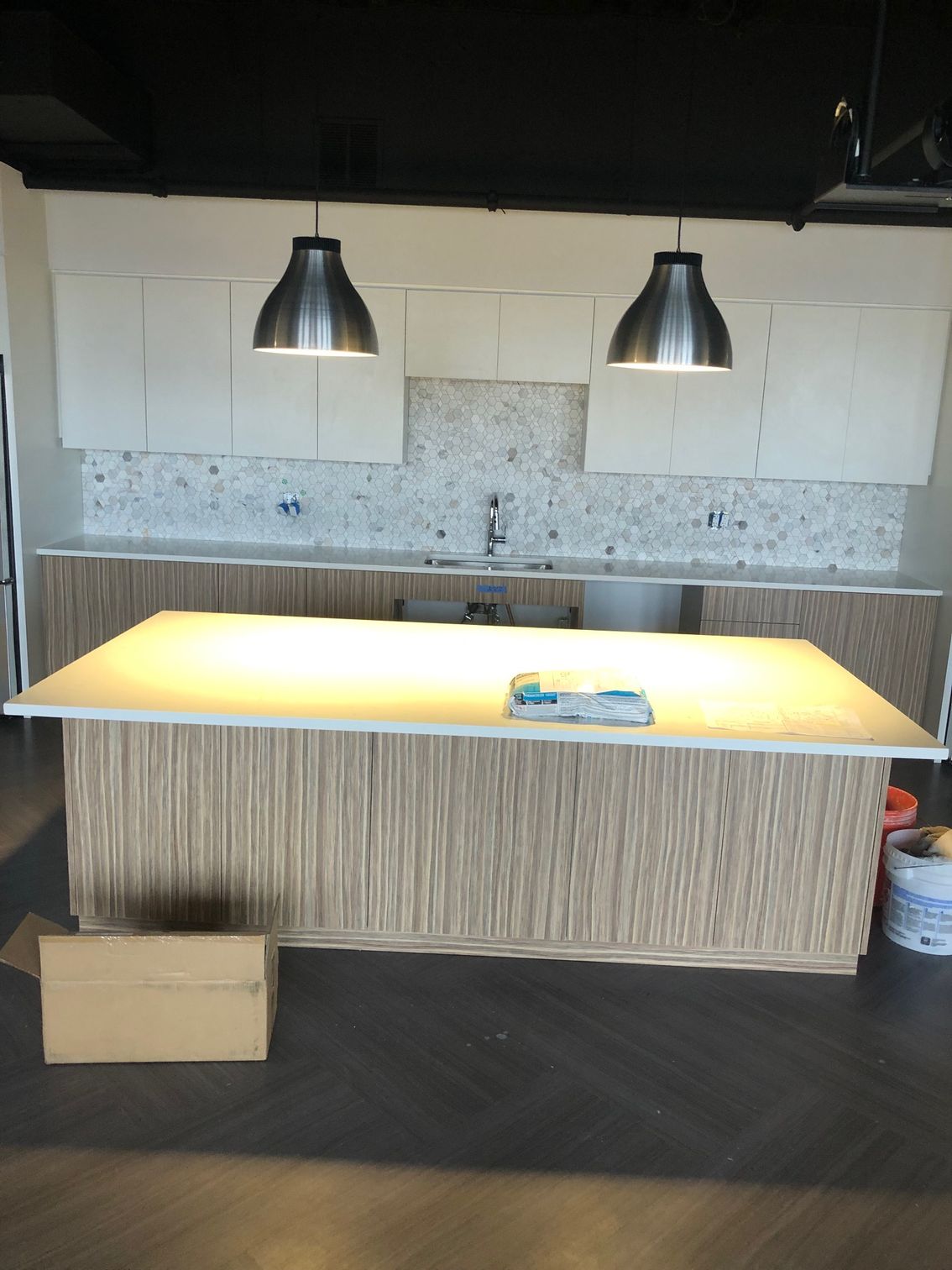 Kitchen with white cabinets, sink, two pendant lights, and a large island in the foreground.