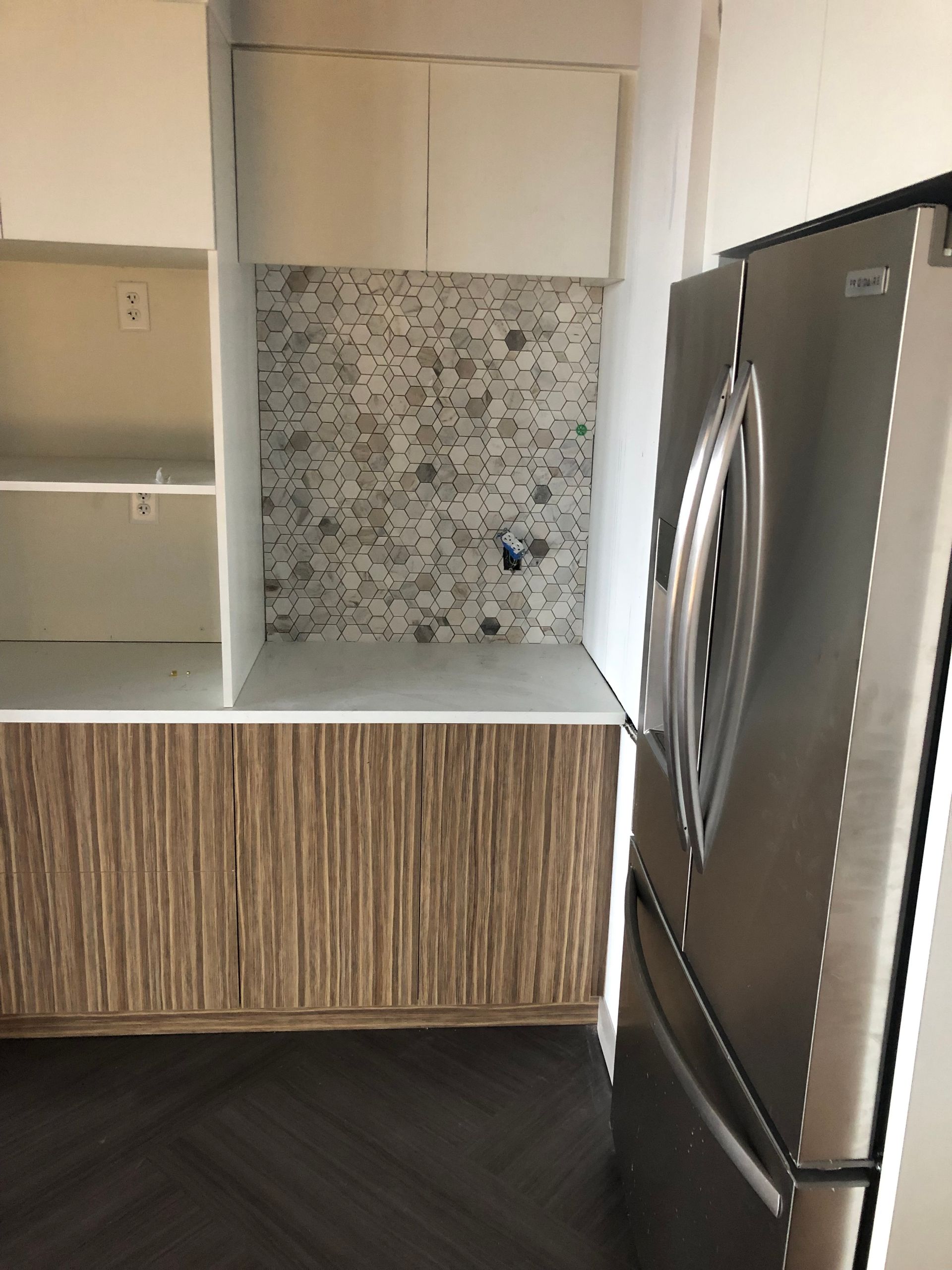 Modern kitchen with white countertops, wood-grain cabinets, mosaic backsplash, and stainless steel refrigerator