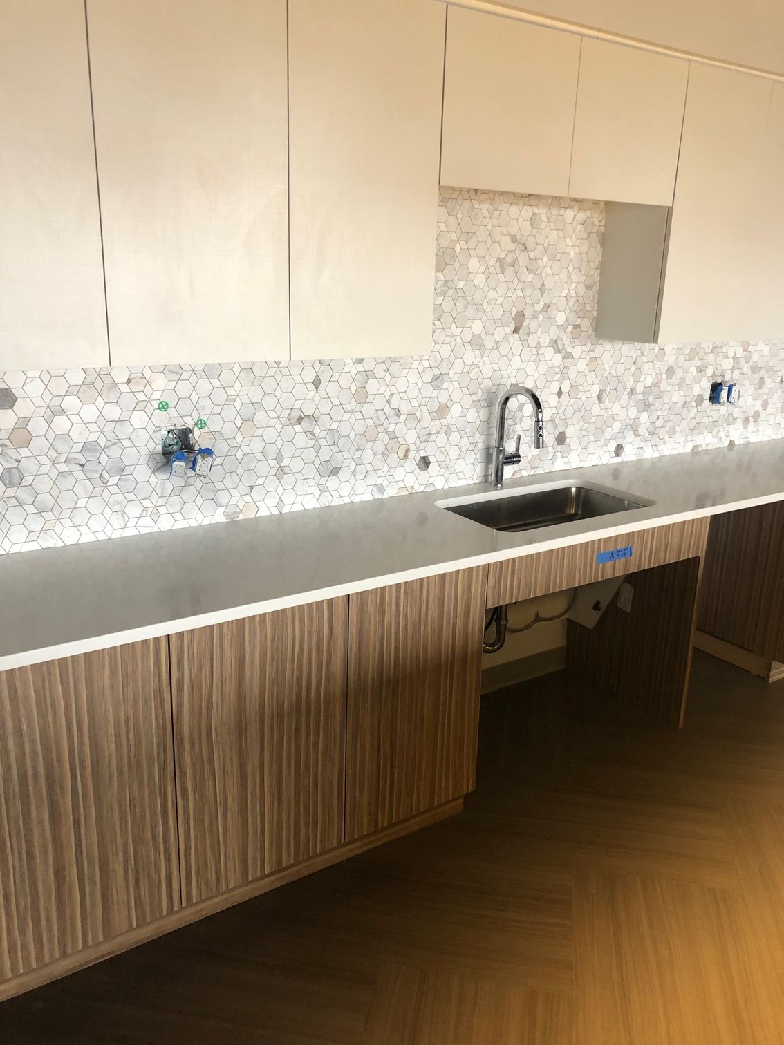 Modern kitchen with wood cabinets, white mosaic backsplash, sink, and large gray countertop