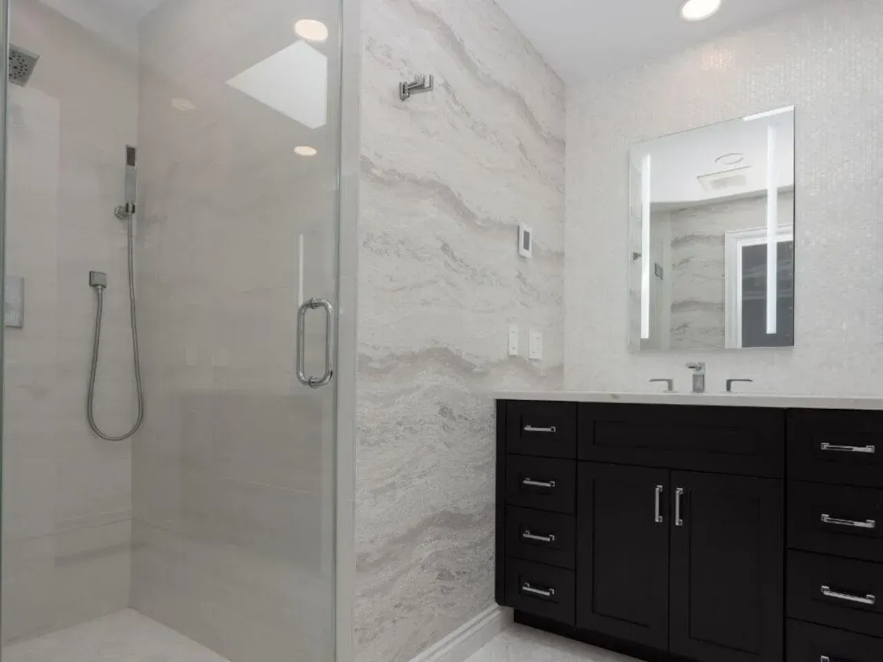 Modern bathroom with a glass shower, dark vanity, and marble-look wall tiles.