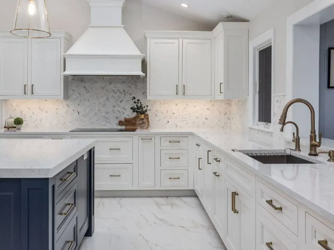 White kitchen with blue island and gold accents, featuring cabinets, countertops, and a range hood.