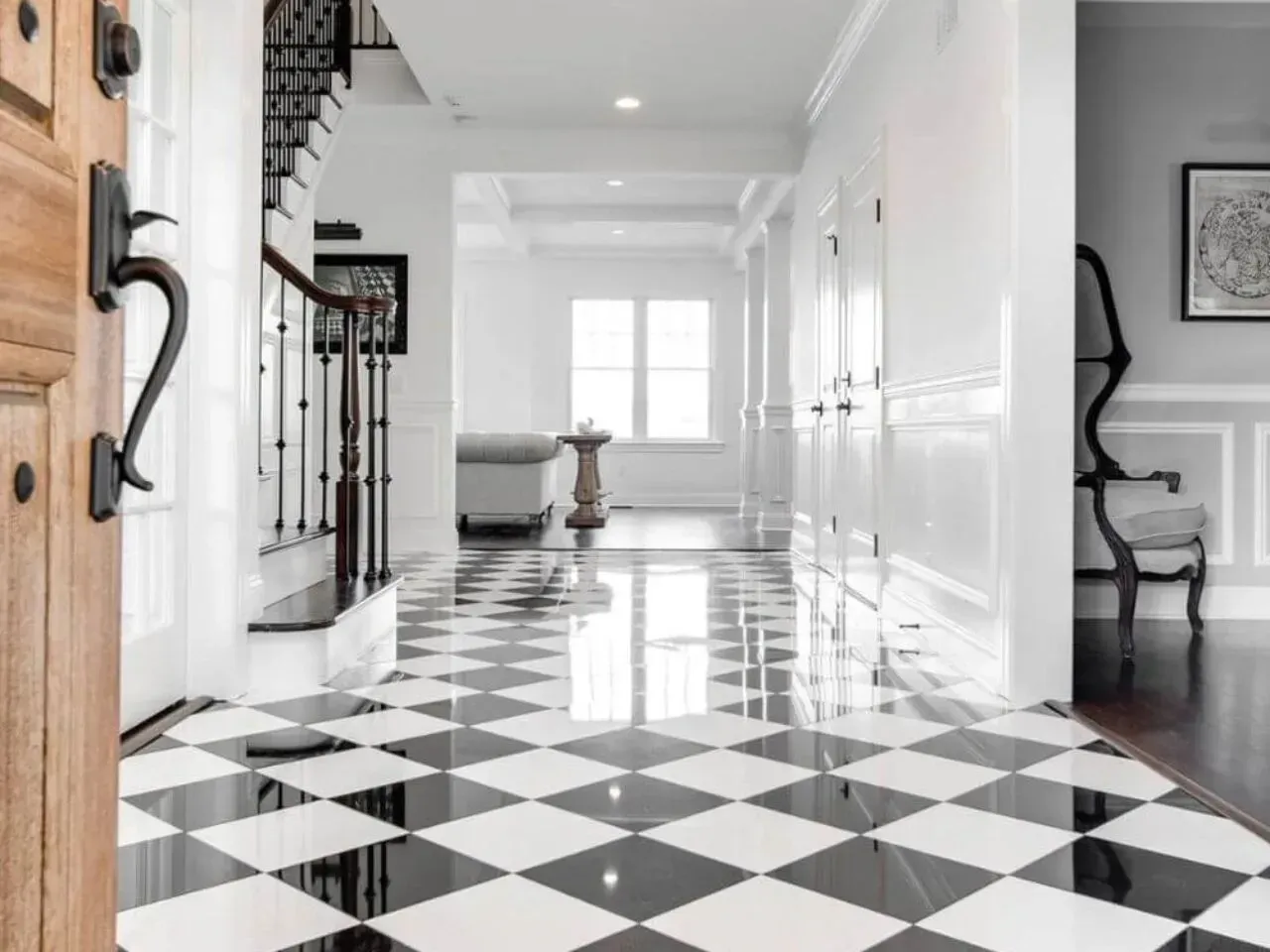 Entryway with black and white checkered floor, white walls, and dark staircase. A wooden door is ajar.