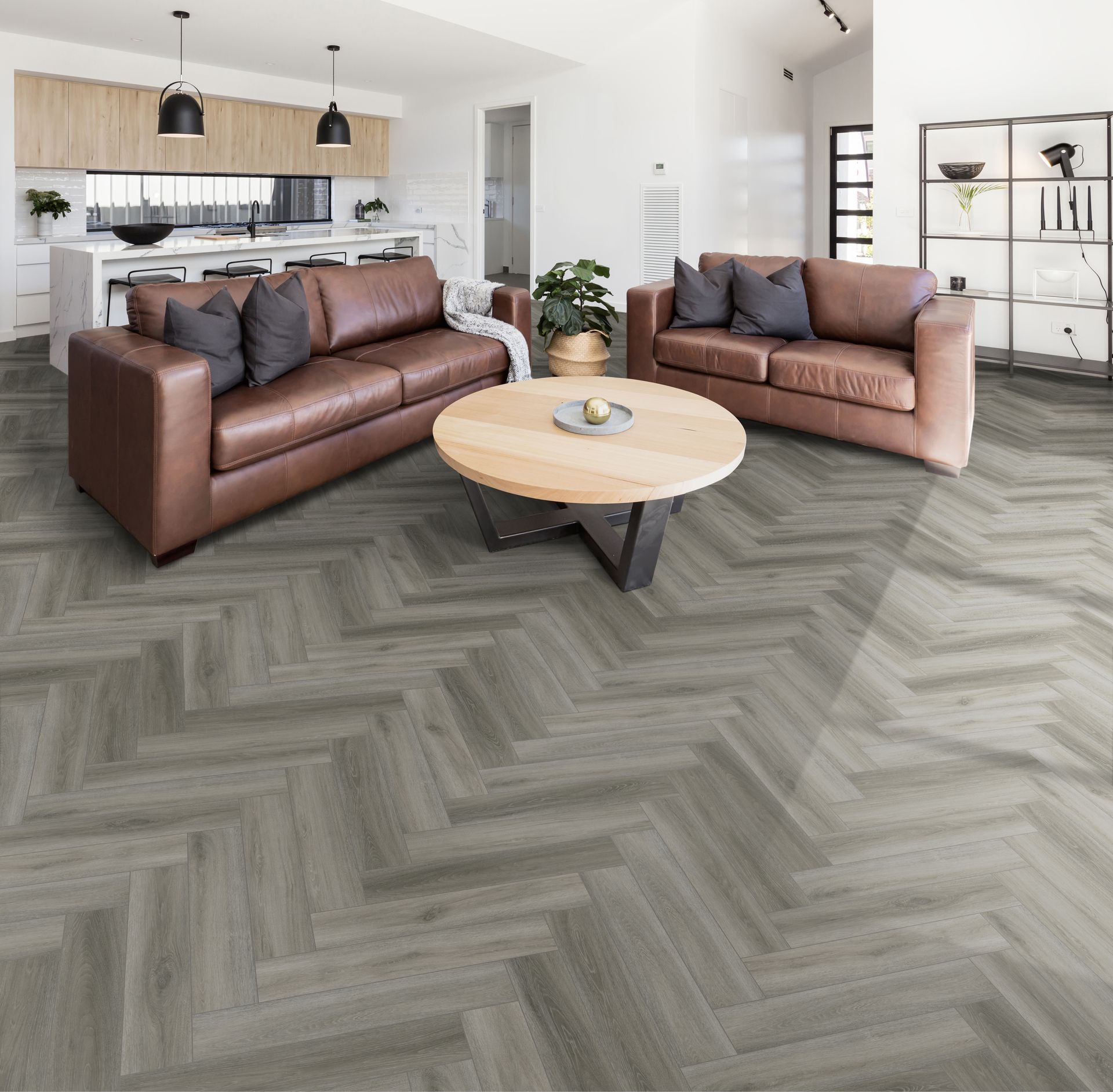 Modern living room with two brown sofas, round coffee table, herringbone floor, and open kitchen in the background