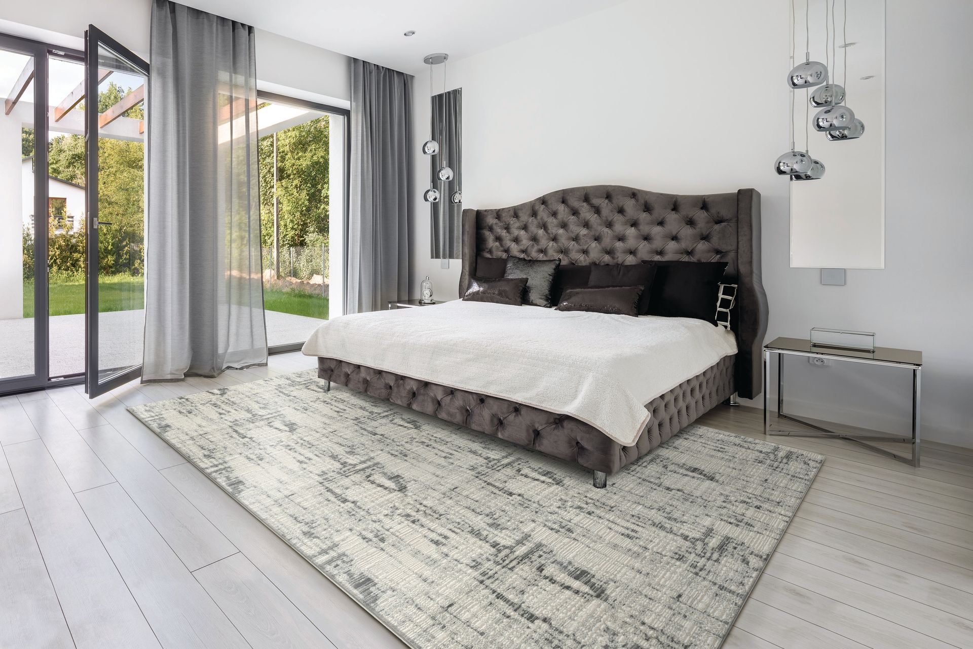 Bedroom with gray velvet bed, light rug, glass doors, and modern pendant lights.