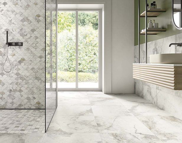 Bathroom with patterned shower tile, marble floor, wooden vanity, and large window overlooking greenery.