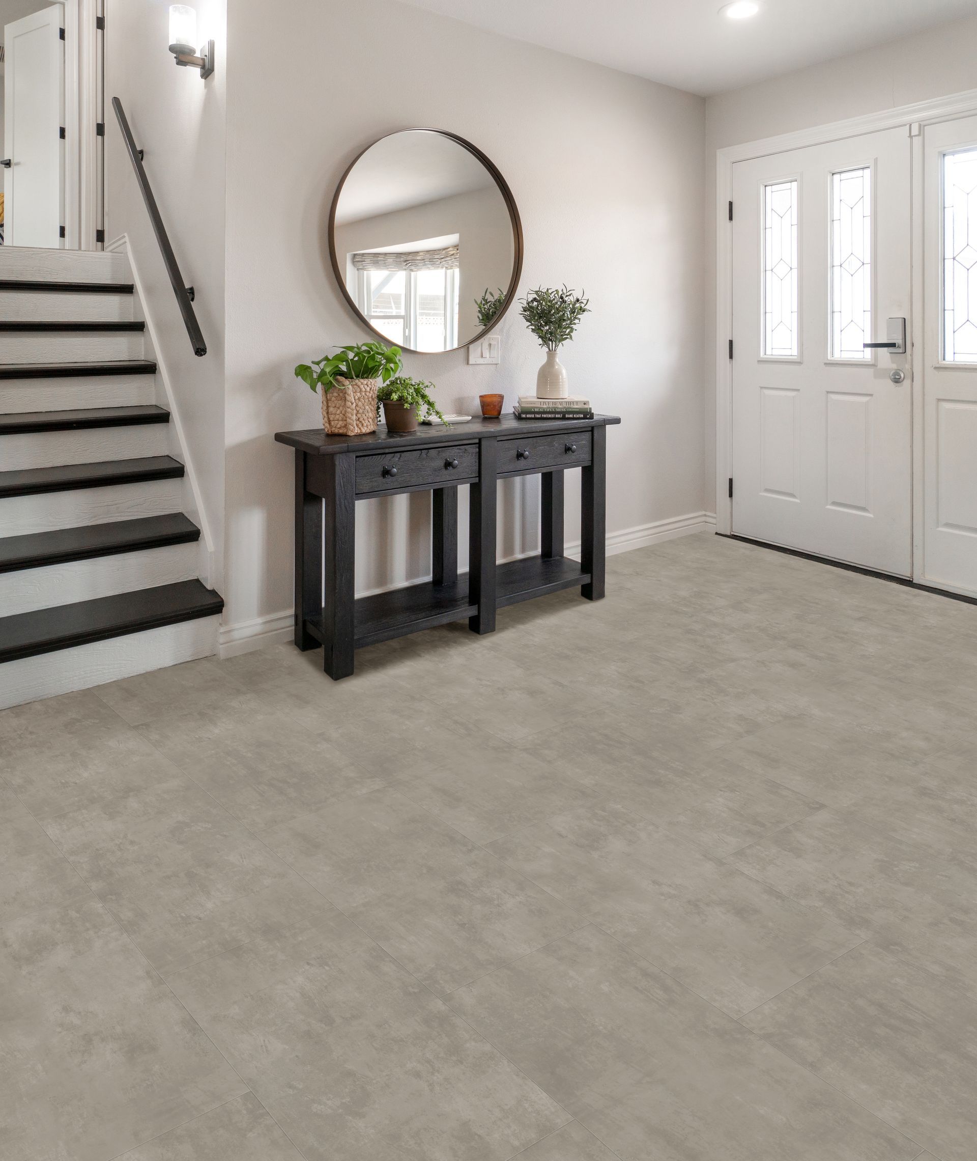 Bright foyer with carpet, staircase, console table, round mirror, and front door