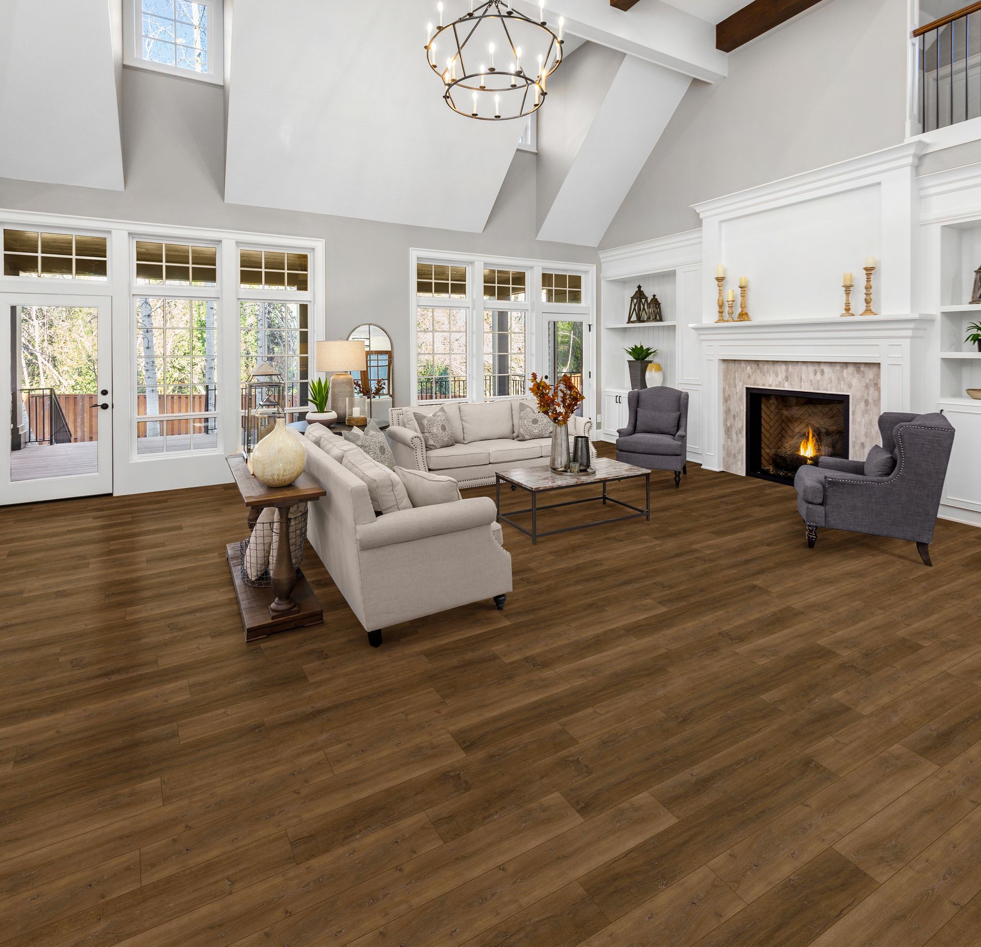 Bright living room with white fireplace, vaulted ceiling, large windows, beige sofa, and dark wood floors