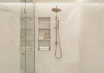 Modern, white-tiled shower with built-in shelves and gold showerhead.