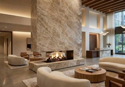 Modern lobby with large marble fireplace, seating, and reception desk. Neutral colors and natural light.