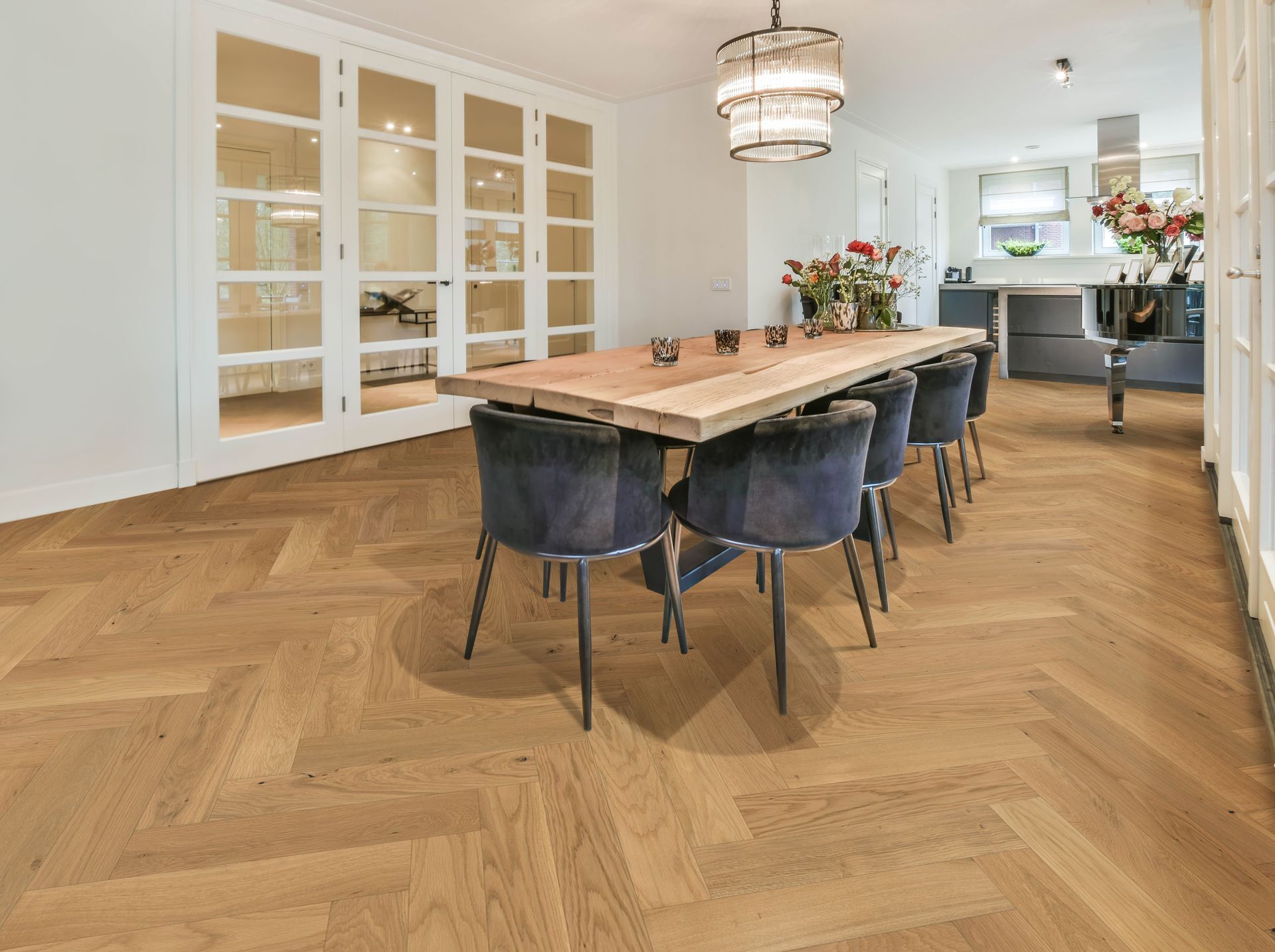 Dining room with wooden herringbone floor, large table with blue chairs, glass-paned doors.
