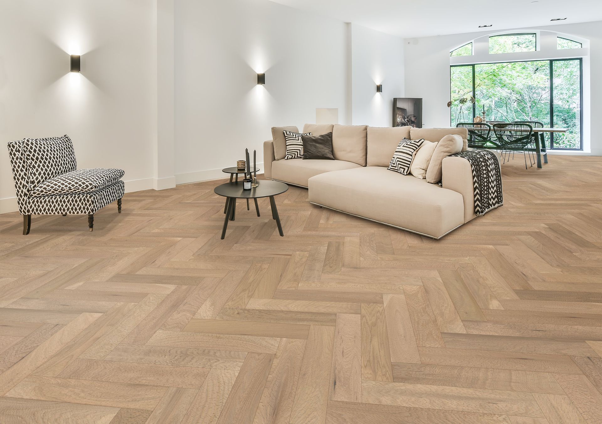 Living room with herringbone wood floor, beige sofa, patterned armchair, and large windows.