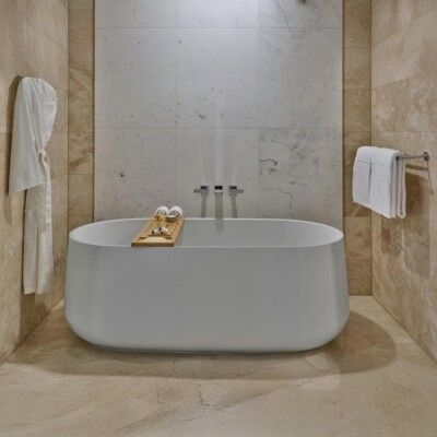 Modern bathroom with white freestanding tub, cream walls, and wooden bath tray.