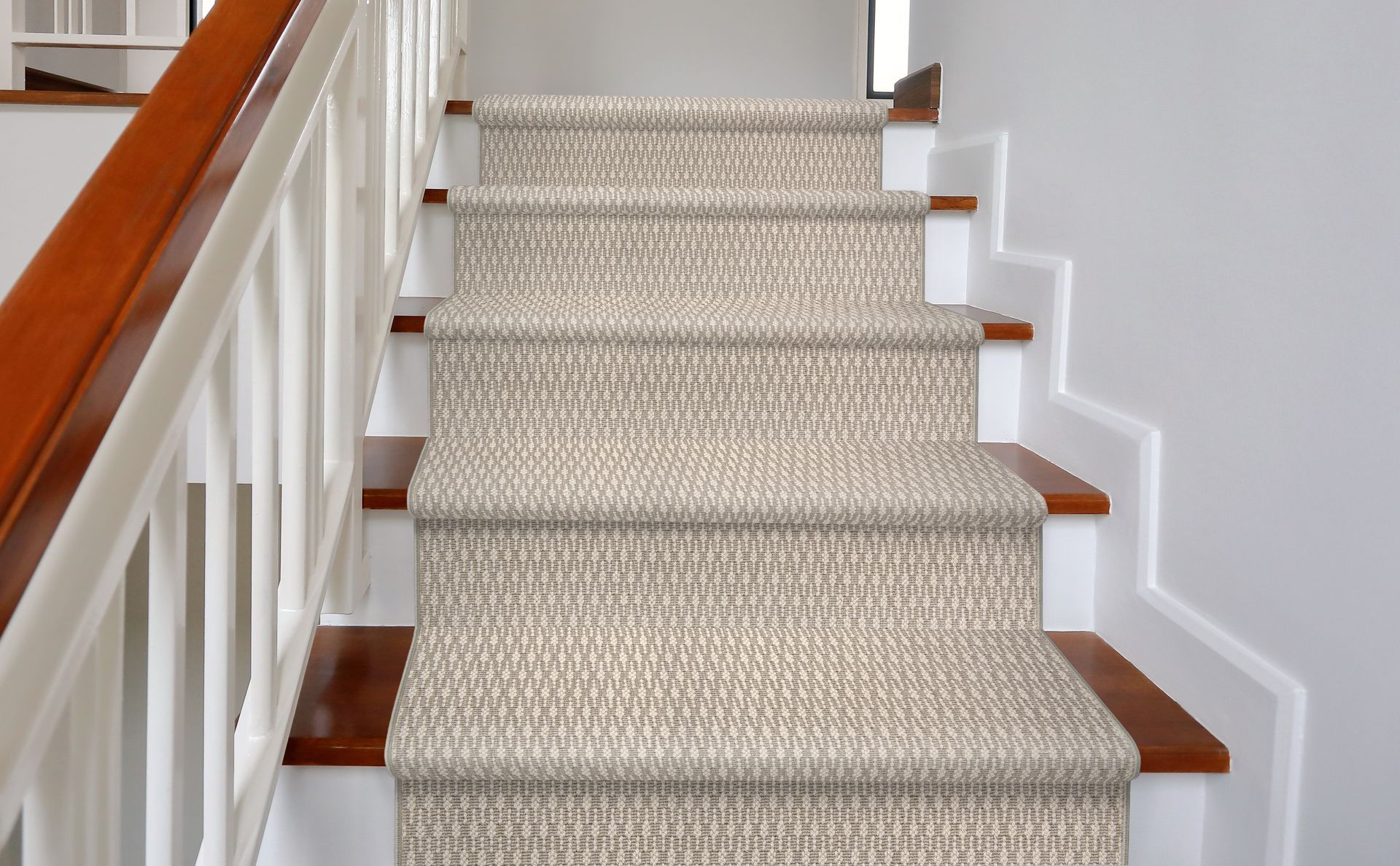 Staircase with carpeted steps in a neutral tone and white railing with wooden handrail.